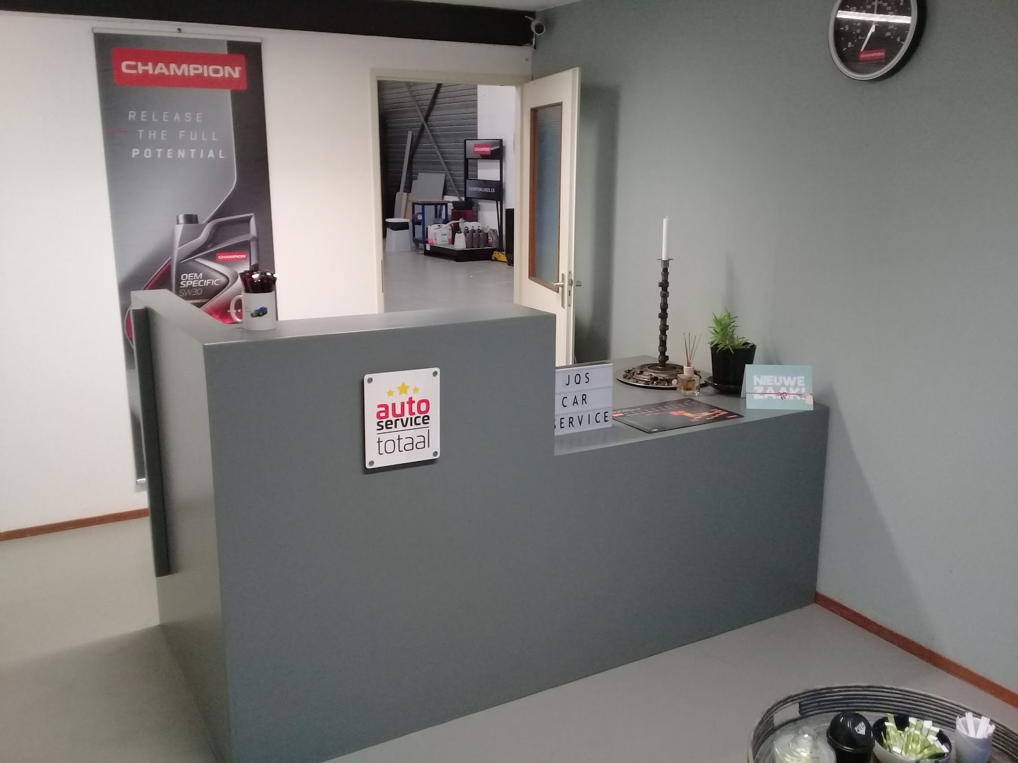 De balie met de letters JQS Car Service, een nokkenas als kandelaar en een plant