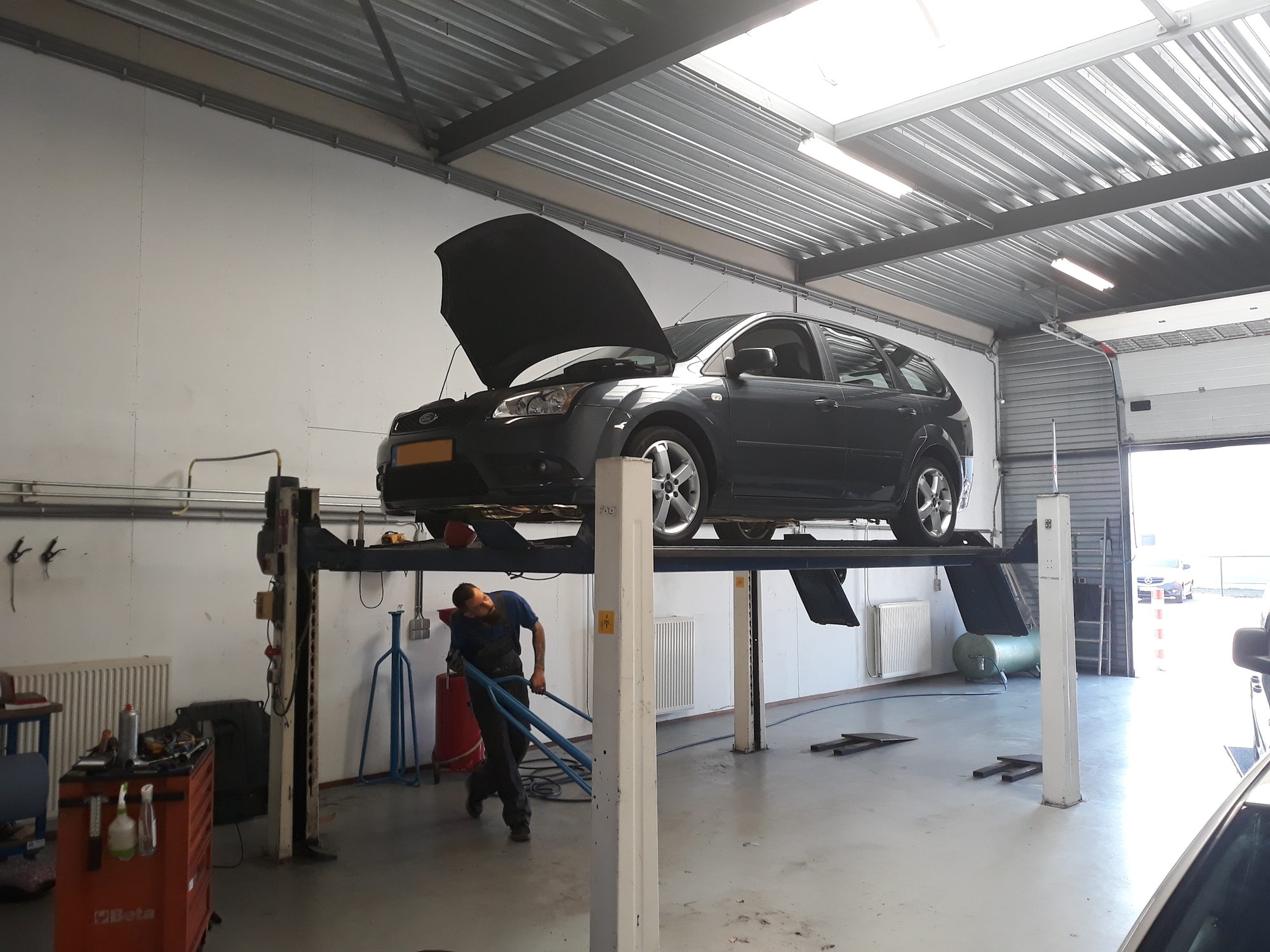 De Ford Focus omhoog op de brug, met de monteur eronder aan het werk